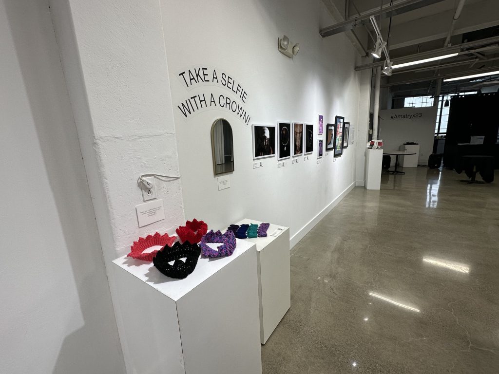 A wall of the exhibition, including the crochet crowns and multiple photos and artworks.