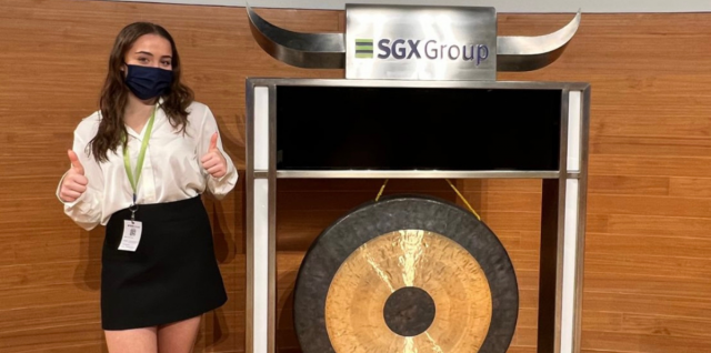 Sarah Sauer, MBA '25, standing in front of the Singapore Stock Exchange gong with thumbs up