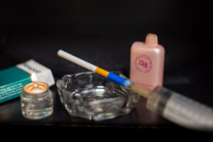 Image captured in Dr. Larry Hawk's research lab in October 2025. The image includes an oil candle and a syringe which are used to light cigarettes in the lab environment, a pack of cigarettes, an ashtray and a vape.