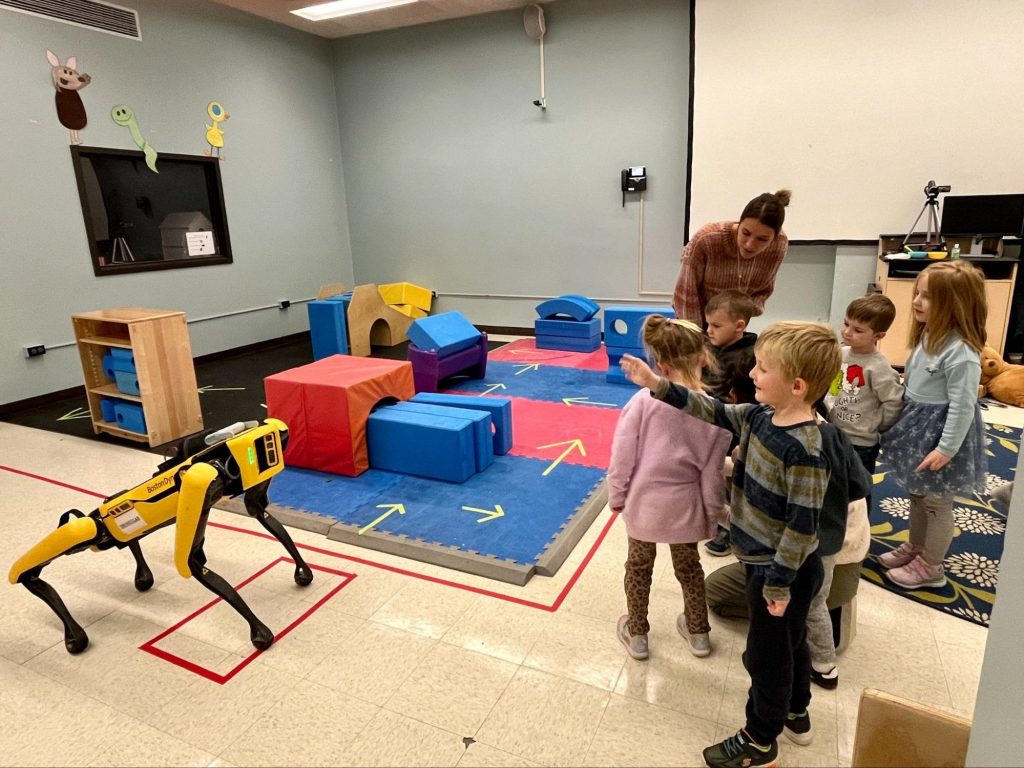 Young children standing in a classroom playing with a robot