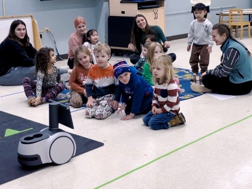 Young children standing in a classroom playing with a robot