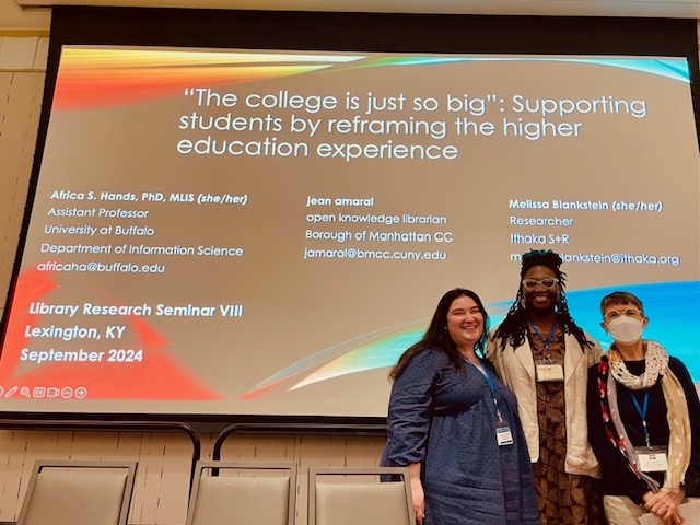 Color group photo of Africa, Melissa, and jean in front of screen displaying PowerPoint slide.