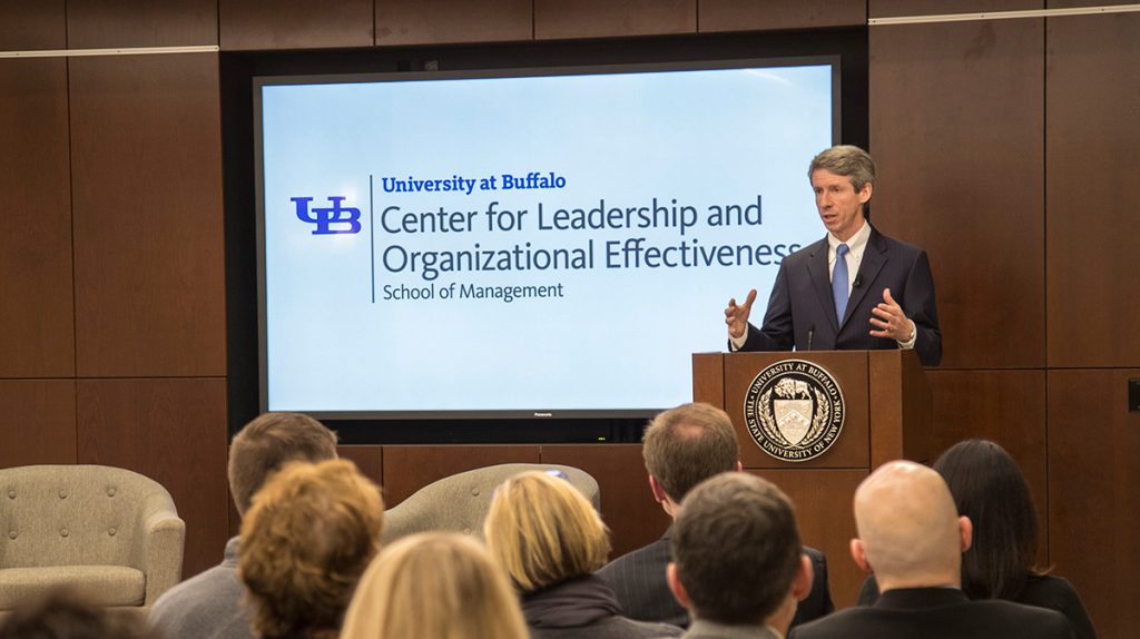 John Scannell in front of a TV screen with the Center for Leadership and Organizational Effectiveness logo on it