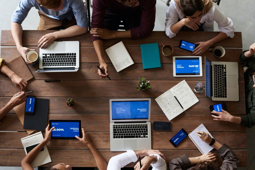 Professionals sitting around a table working on laptops, tablets and notepads.